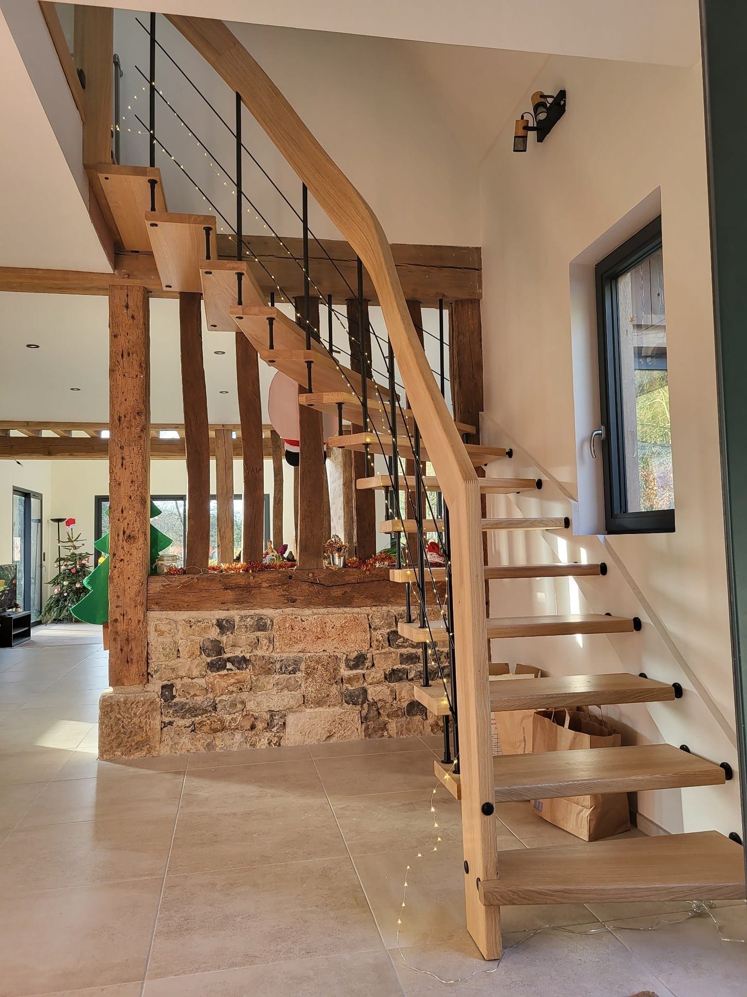 Escalier moderne avec des marches en bois et une structure en métal noir, accompagné d'une rampe en bois courbé, situé à côté d'un mur de pierres.