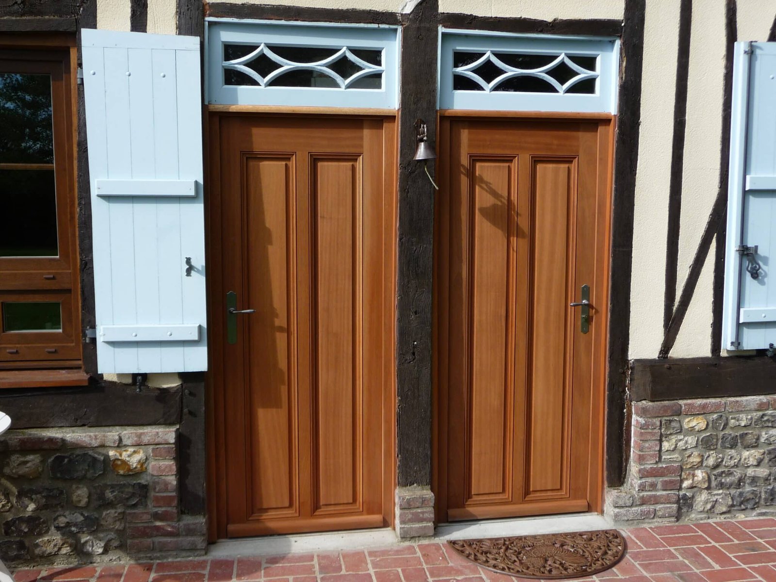 Deux portes en bois marron, montées dans une structure avec poutres en bois et murs en briques apparentes.