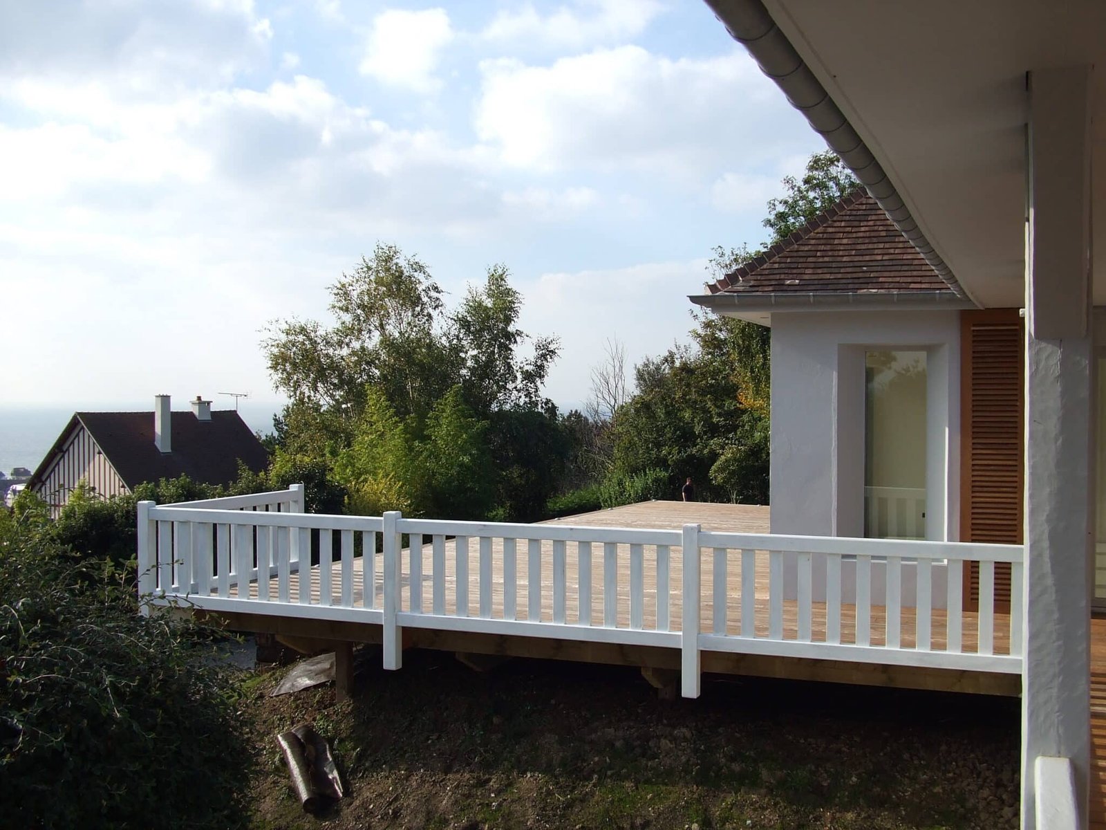 Grande terrasse en bois surélevée avec garde-corps blancs, offrant une vue dégagée sur les environs.