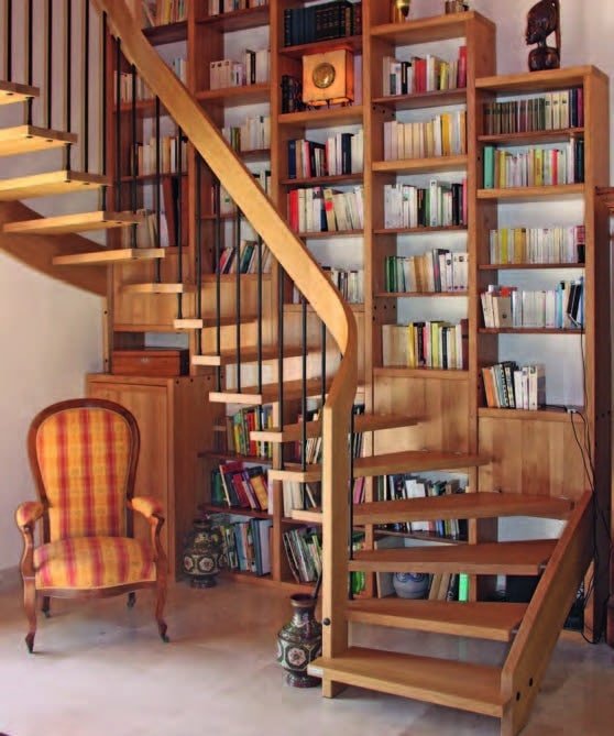 Escalier en bois intégré dans une bibliothèque classique avec fauteuil et décorations