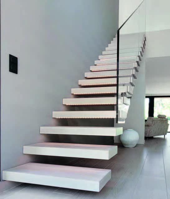 Un escalier flottant en bois blanc avec éclairage LED et une rampe en verre transparent. L'escalier se trouve dans un intérieur moderne avec un sol en bois clair et des murs gris.