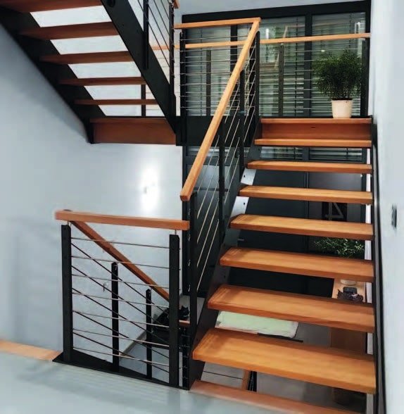 Escalier contemporain avec des marches en bois et une rampe en métal noir, situé dans une maison moderne avec une grande baie vitrée.