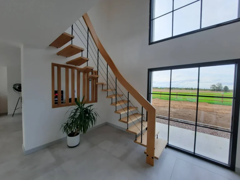 Escalier tournant à marches bois et garde-corps métal devant une baie vitrée